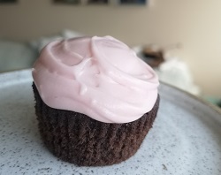 A chocolate cupcake with pale pink icing on a while plate
